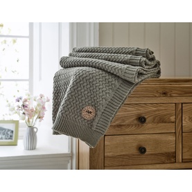 The Lyndon Company Cadenza Throw in grey, chunky cable-knit texture with wooden button detail, draped over a wooden chest of drawers
