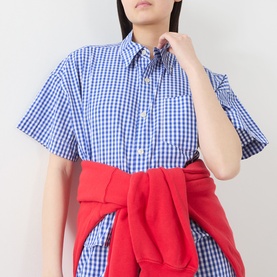 Model wearing American Vintage shirt in Vichy Bleu gingham check, short sleeves, button-down collar, styled with red knotted sweatshirt at waist