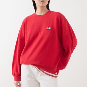 Model wearing American Vintage red cotton sweat top with small chest embroidery, styled with white trousers and striped hem detail.