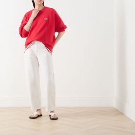 Model wearing American Vintage red cotton sweat top, styled with white wide-leg trousers and dark sandals.