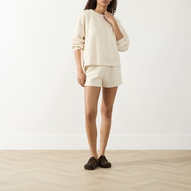 Model wearing American Vintage Bobypark Textured Sweatshirt in ecru, styled with matching ecru shorts and dark loafers.
