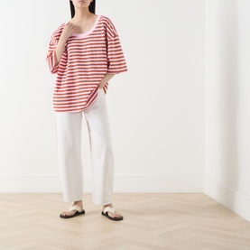 Model wearing American Vintage T-Shirt in Rayures Bonbon red and white stripe, with white trousers and brown sandals.