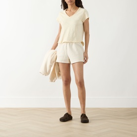 Model wearing American Vintage Sonoma T-Shirt in Vanille Vintage, styled with matching shorts and dark slip-on shoes, holding a cream scarf