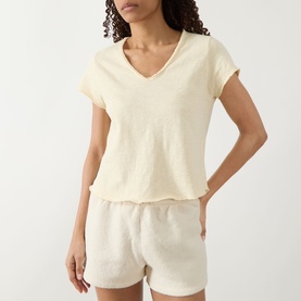 Model wearing American Vintage Sonoma T-Shirt in Vanille Vintage, V-neck, short sleeves, raw-edge hem, styled with matching shorts.