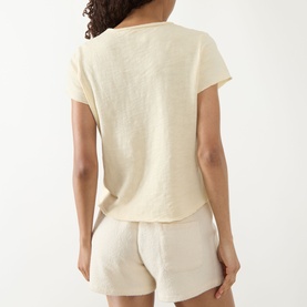 Model wearing American Vintage Sonoma T-Shirt in Vanille Vintage, back view, styled with cream linen shorts. V-neck, short sleeves, straight hem.