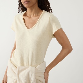 Model wearing American Vintage Sonoma T-Shirt in Vanille Vintage, V-neckline, raw edges, slub texture, styled with cream trousers