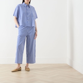 Model wearing AMERICAN VINTAGE trousers in Vichy Bleu cotton stripe, styled with matching short-sleeve shirt and beige loafers.
