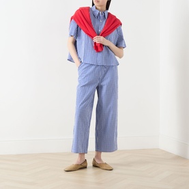 Model wearing AMERICAN VINTAGE Vichy Bleu check cotton trousers, styled with matching shirt and red sweater draped over shoulders.