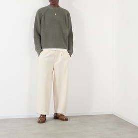 Model wearing About:Blank Logo Rib Knit Sweater in sage, crew neck, styled with cream wide-leg trousers and brown loafers.