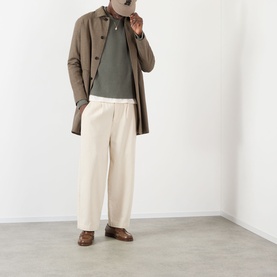 Model wearing About:Blank Logo Rib Knit Sweater in sage, styled with a brown overcoat, cream wide-leg trousers and brown loafers.