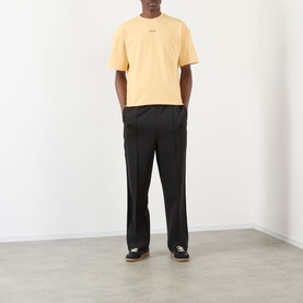 Model wearing About:Blank Raw Hem Ellipse T-Shirt in yellow with black wide-leg trousers and dark trainers.