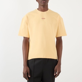 Model wearing About:Blank Raw Hem Ellipse T-Shirt in yellow cotton, with round neck and small logo detail, styled with black trousers.
