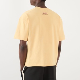 Model wearing About:Blank Raw Hem Ellipse T-Shirt in yellow, rear view showing logo detail, styled with black joggers.
