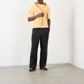 Model wearing About:Blank Raw Hem Ellipse T-Shirt in yellow, styled with black wide-leg trousers and dark loafers.