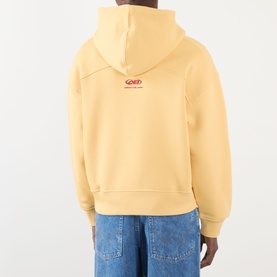 Model wearing About:Blank Arc Logo Hoodie in yellow, back view showing red logo print, fixed hood, and relaxed fit, styled with blue jeans.