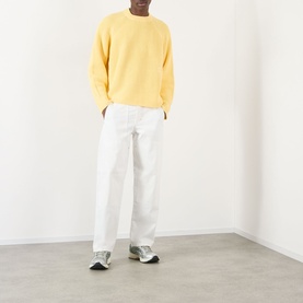 Model wearing About:Blank Logo Rib Knit Sweater in yellow, crew neck, styled with white wide-leg trousers and grey trainers.