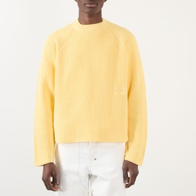 Model wearing About:Blank Logo Rib Knit Sweater in yellow, crew neck, ribbed cotton with logo badge, styled with white trousers.