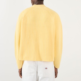 Model wearing About:Blank Logo Rib Knit Sweater in yellow, crew neck, ribbed cotton knit, long sleeves, rear view, styled with white trousers.