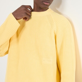 Model wearing About:Blank Logo Rib Knit Sweater in yellow, featuring crew neckline, ribbed texture and subtle logo badge detail.