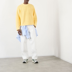 Model wearing About:Blank Logo Rib Knit Sweater in yellow, styled with white wide-leg trousers and a light blue shirt tied at the waist.