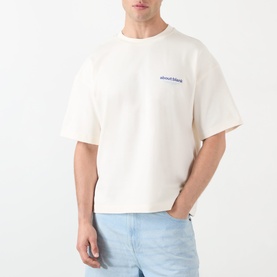 Model wearing About:Blank oat cotton T-shirt with blue logo print, styled with light blue jeans