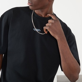Model wearing About:Blank Raw Hem Ellipse T-Shirt in washed black, styled with a silver chain necklace, showing chest logo detail.