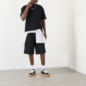 Model wearing About:Blank Raw Hem Ellipse T-Shirt in washed black, styled with white shirt, black shorts, and gum-sole trainers.
