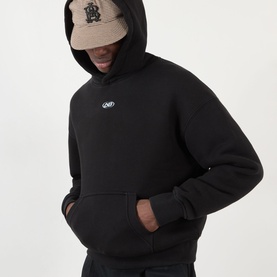 Model wearing About:Blank Arc Logo Hoodie in black with fixed hood, kangaroo pocket, and small chest logo. Styled with a beige cap.
