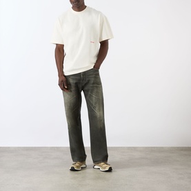Model wearing About:Blank Haus Logo T-Shirt in oat/red with dark olive distressed jeans and beige trainers.