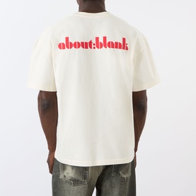 Model wearing About:Blank Haus Logo T-Shirt in oat, rear view showing red logo print, with distressed jeans