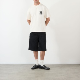 Model wearing About:Blank oat cotton T-shirt with chest graphic, styled with black shorts, white socks and black loafers