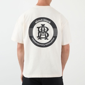 Model wearing About:Blank oat cotton T-shirt, back view showing circular brand graphic print with monogram logo