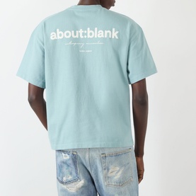 Model wearing About:Blank Box Logo T-Shirt in tourmaline, back view showing white logo print, styled with distressed light-wash jeans.
