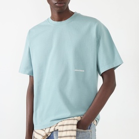 Model wearing About:Blank Box Logo T-Shirt in tourmaline/ecru, crew neck, short sleeve, styled with a checked shirt tied at the waist.