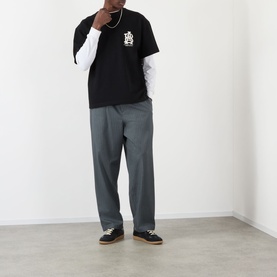 Model wearing About:Blank black cotton T-shirt layered over white long-sleeve top, styled with grey trousers and dark trainers.