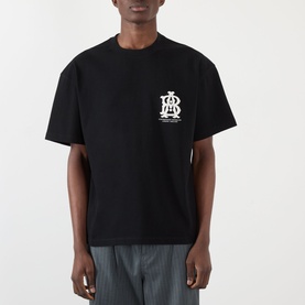 Model wearing About:Blank black cotton T-shirt with white monogram logo print on chest, styled with grey striped trousers