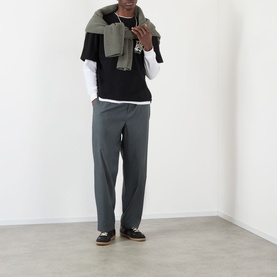 Model wearing About:Blank black cotton T-shirt, layered over white long-sleeve top, styled with grey trousers and a draped khaki scarf.