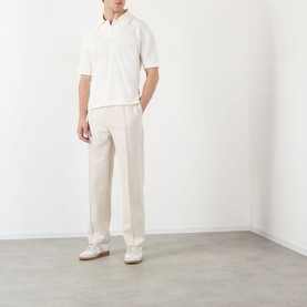 Model wearing cream wide-leg trousers styled with a white short-sleeve polo shirt and white trainers.