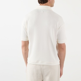 Model wearing a white short-sleeve knit polo shirt, rear view, styled with light beige trousers.