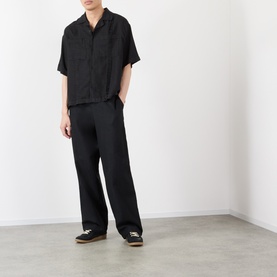 Model wearing black wide-leg trousers styled with a black short-sleeve shirt and dark canvas shoes