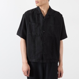 Model wearing black short-sleeve open-collar shirt with tonal patchwork detailing and chest pockets, styled with black trousers