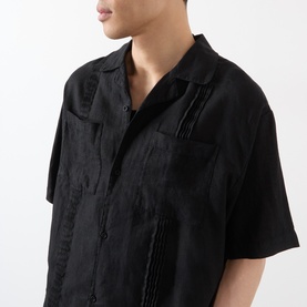 Model wearing black short-sleeve shirt with tonal embroidered detail and open collar, cropped side view