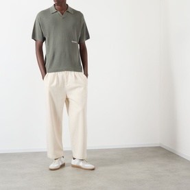 Model wearing About:Blank Logo Open-Knit Polo Sweater in sage with cream wide-leg trousers and white trainers.