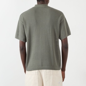 Model wearing About:Blank Logo Open-Knit Polo Sweater in sage, short sleeves, open-knit construction, paired with cream trousers. Back view.