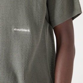 Model wearing About:Blank Logo Open-Knit Polo Sweater in sage, close-up showing open-knit texture and contrast logo detail