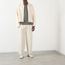 Model wearing About:Blank Logo Open-Knit Polo Sweater in sage, styled with cream zip jacket and wide-leg trousers, white trainers.