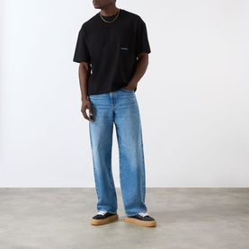 Model wearing About:Blank Box Logo T-Shirt in black with blue wide-leg jeans and navy canvas trainers with tan soles.