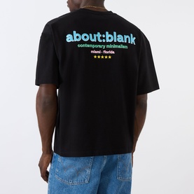 Model wearing About:Blank Box Logo T-Shirt in black, rear view showing multicolour logo print, paired with light blue jeans.