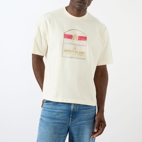 Model wearing About:Blank Graphic Logo T-Shirt in oat, featuring front logo graphic print, crew neck and short sleeves, styled with blue jeans