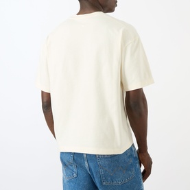 Model wearing About:Blank Graphic Logo T-Shirt in oat, rear view, crew neck, dropped shoulders, styled with blue jeans.